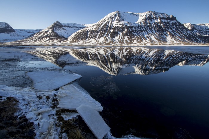 Snow-covered mountains reflected in a calm lake with ice