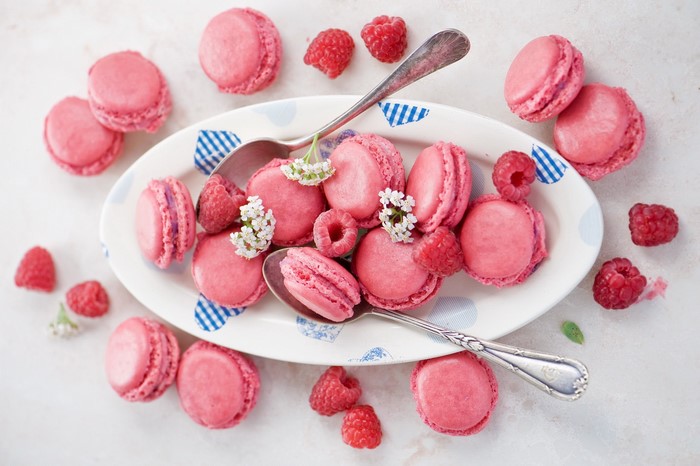 Pink macarons with raspberries on a plate with spoons