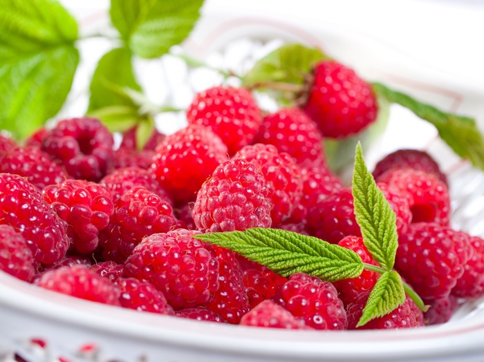 Raspberries in a bowl with green leaves