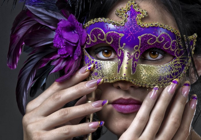 Woman wearing a purple and gold masquerade mask with feathers