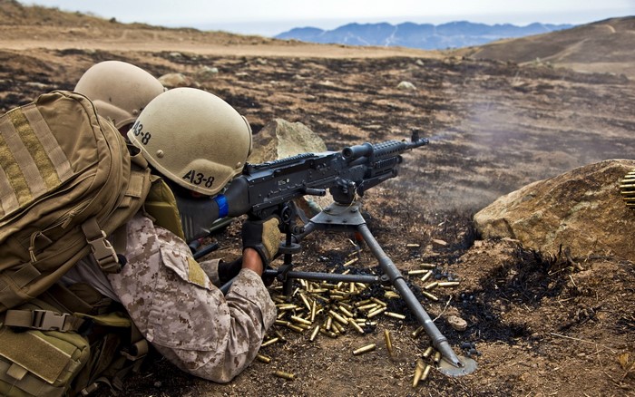 Marines firing a machine gun in a dry, hilly landscape