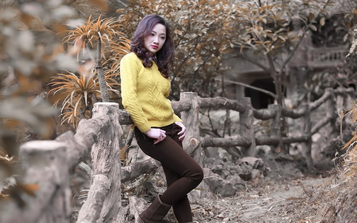 Asian woman in yellow sweater leaning on fence