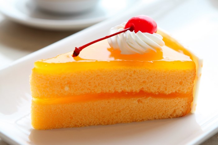 Slice of orange cake with cherry and whipped cream