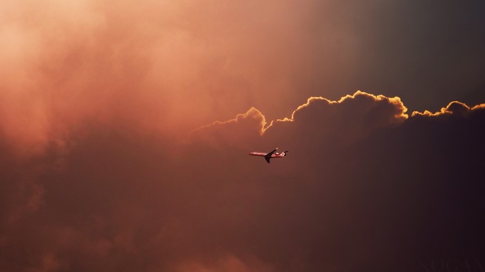 Airplane flying through dramatic sunset clouds