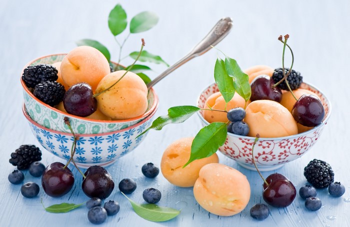 Bowls of fresh apricots, cherries, blueberries, and blackberries