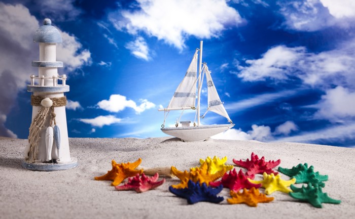 Toy lighthouse, sailboat, and starfish on sand with sky background