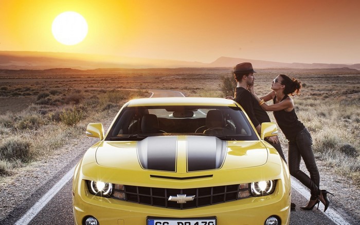 Yellow Chevrolet Camaro with a couple at sunset