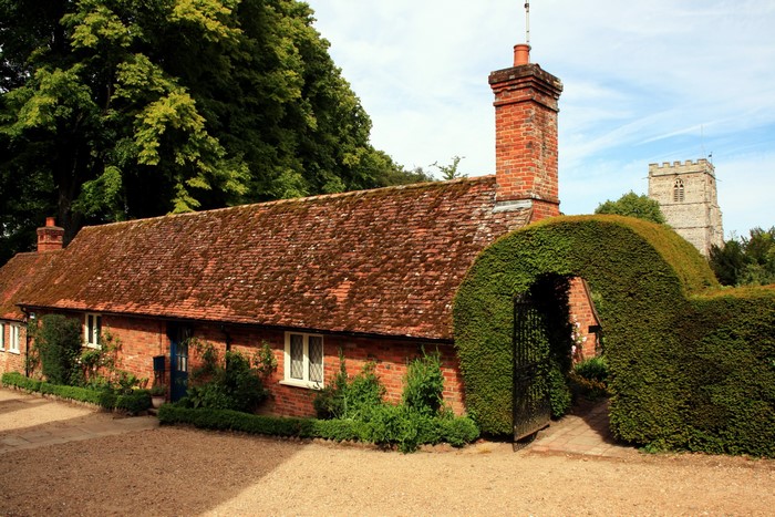 Brick cottage with arched hedge and church tower in Cranborne, England