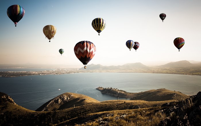 Hot air balloons flying over a bay and mountains