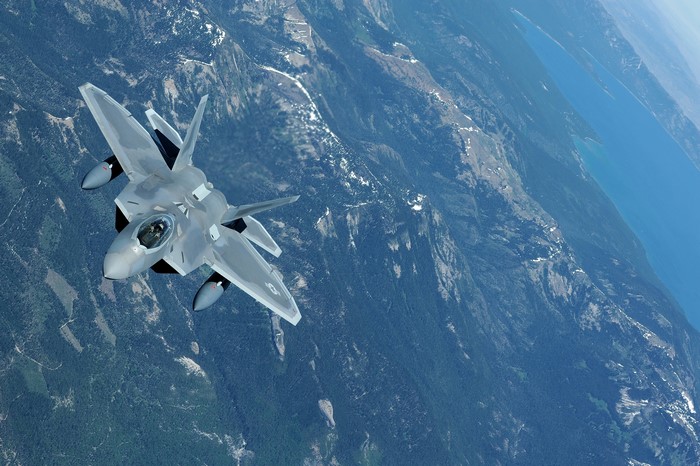 US Air Force F-22A Raptor flying over mountains and lake