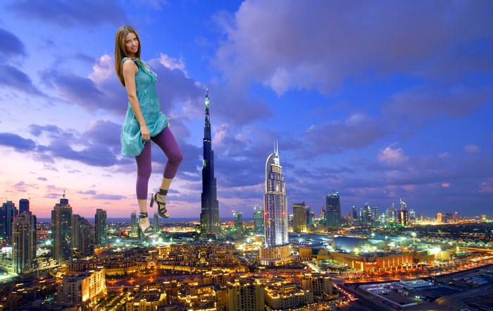 Giant woman standing over Dubai skyline at dusk