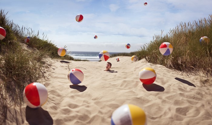 Boy buried in sand with beach balls on a beach
