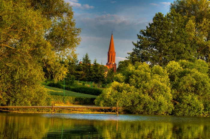 Church tower over trees by a lake in Gmina Cekcyn, Poland