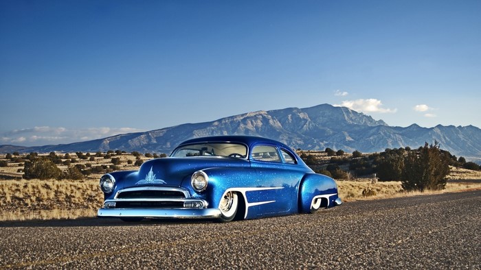 Blue Chevrolet hot rod in a desert landscape with mountains
