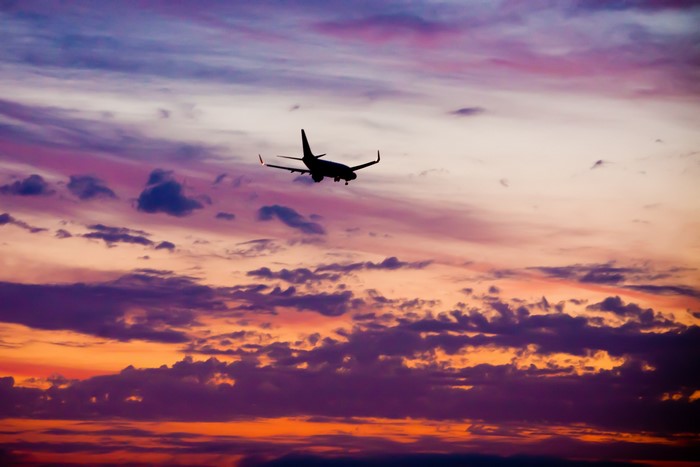 Airplane flying through a colorful sunset sky