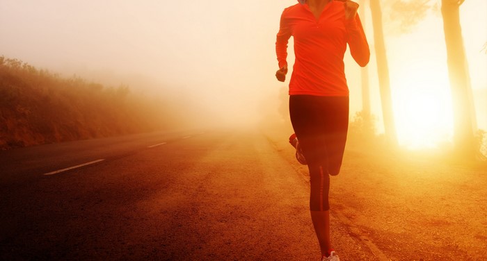 Woman running on a foggy road at sunrise