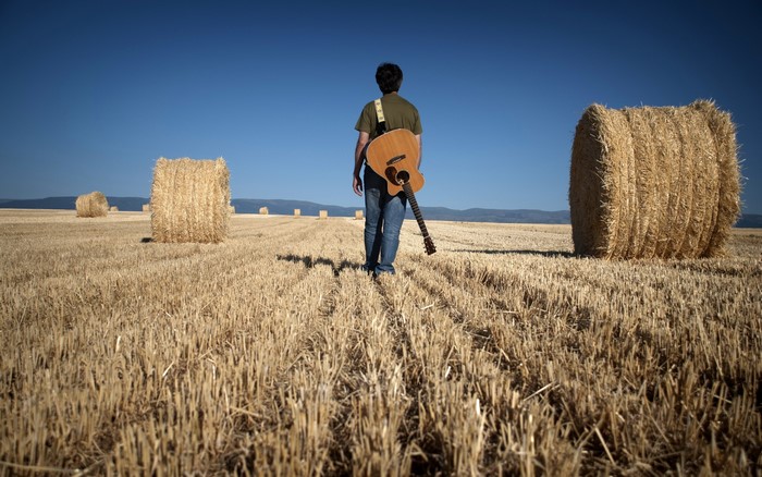 Man with guitar in a field of hay bales