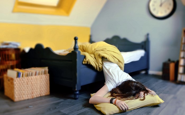 Person sleeping on floor next to bed