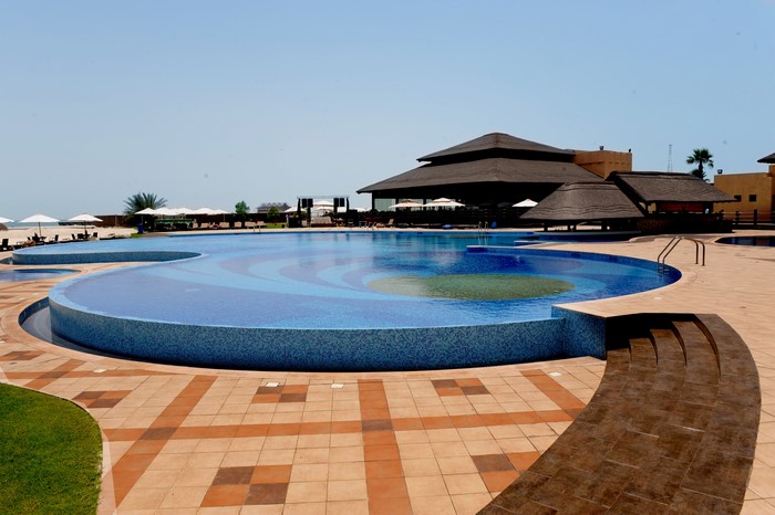Resort swimming pool with tiled steps and thatched roof buildings