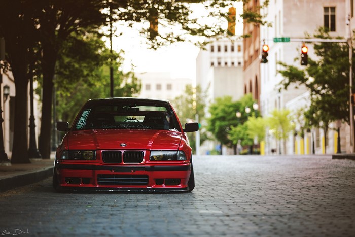 Red BMW E36 parked on a cobblestone street