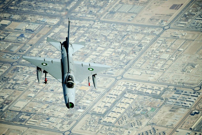 Chengdu J-7 fighter jet flying over a city