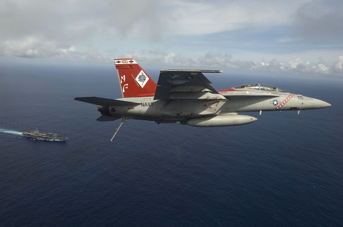 FA-18F Super Hornet flies over the ocean near an aircraft carrier