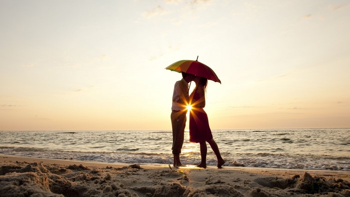 Couple kissing under umbrella on beach at sunset