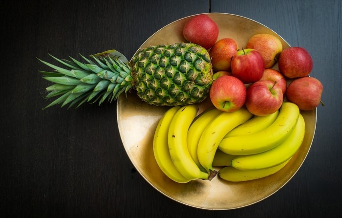 A bowl of fruit with pineapple, bananas, and apples