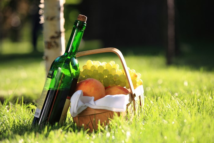 Bottle of Wine with Grapes and Peaches in Basket on Grass
