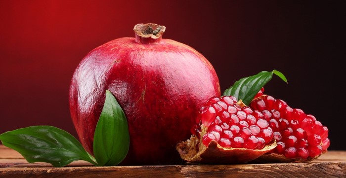 Whole and cut pomegranate with leaves on wooden surface