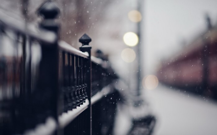Snow falling on a black fence