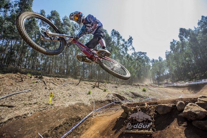 Mountain biker jumping over a dirt track with trees in background