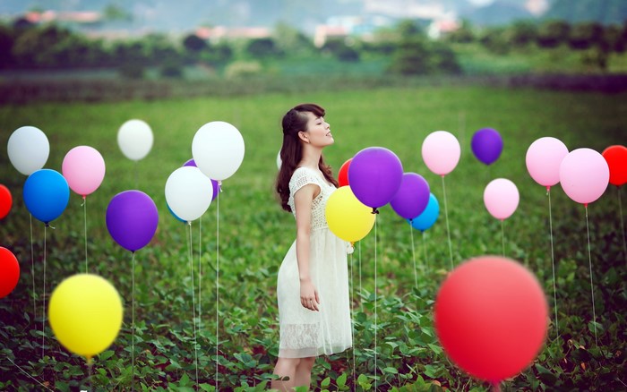 Asian woman in white dress with balloons in a field