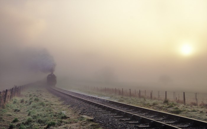 Steam train in fog on railroad tracks