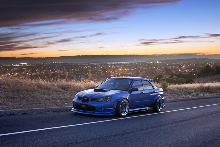 Blue Subaru STI on a road overlooking a city at sunset
