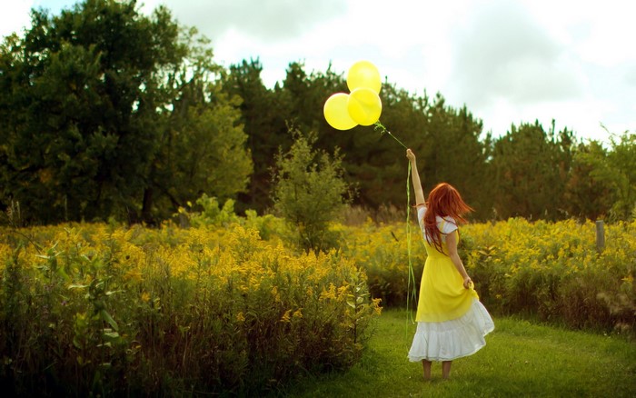 Girl in yellow dress holding balloons in a field