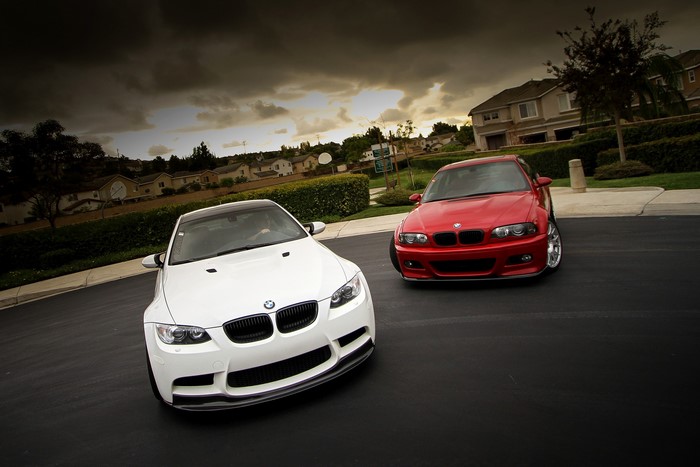 Two BMW M3 cars, white and red, parked on a street