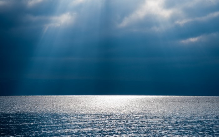 Sunlight beams through clouds onto the ocean horizon