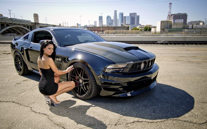 Woman posing with a black Ford Mustang