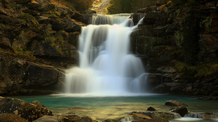 Cascading waterfall over mossy rocks into a turquoise pool