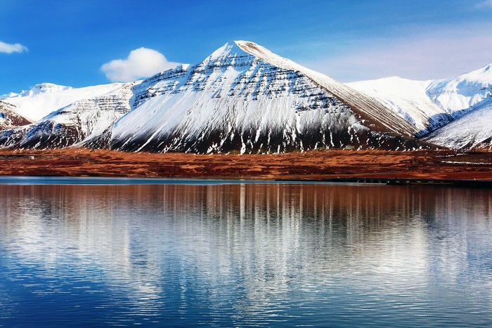Snow-capped Hafnarfjall mountains reflected in water in Iceland