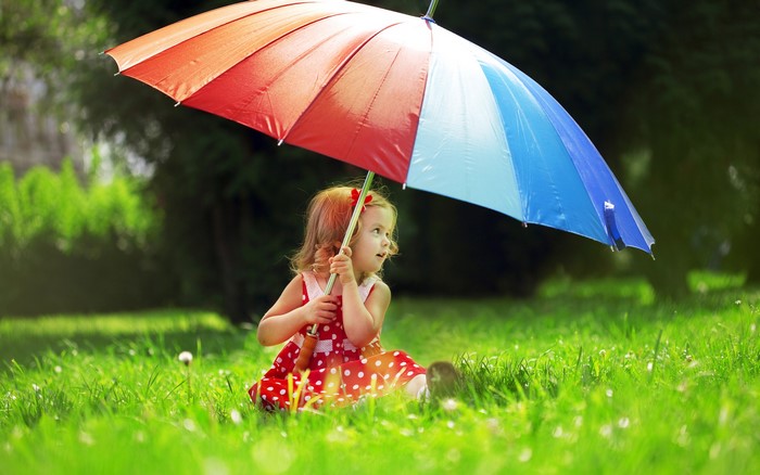 Girl with a colorful umbrella sitting in grass