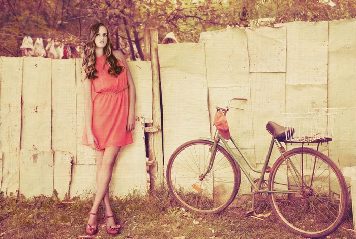 Woman in dress with bicycle by fence