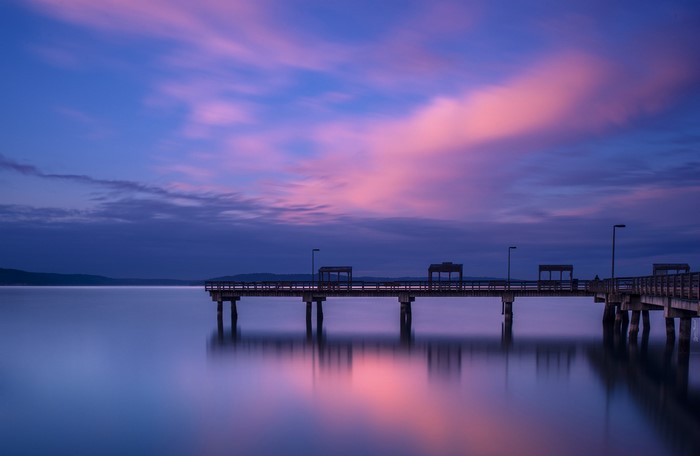 Pier over calm water at twilight with pink clouds