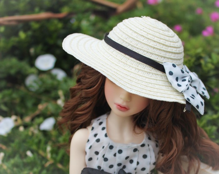 Doll wearing a straw hat with polka dot ribbon