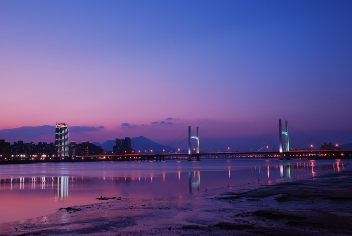 Bridge over river at dusk with city skyline