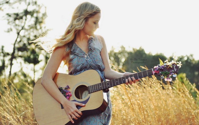 Blonde girl playing guitar in a field