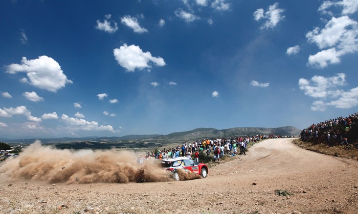 Rally car kicking up dust with spectators