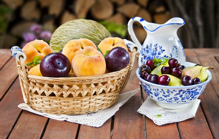 Basket of peaches, plums, and melon with a bowl of cherries and pears