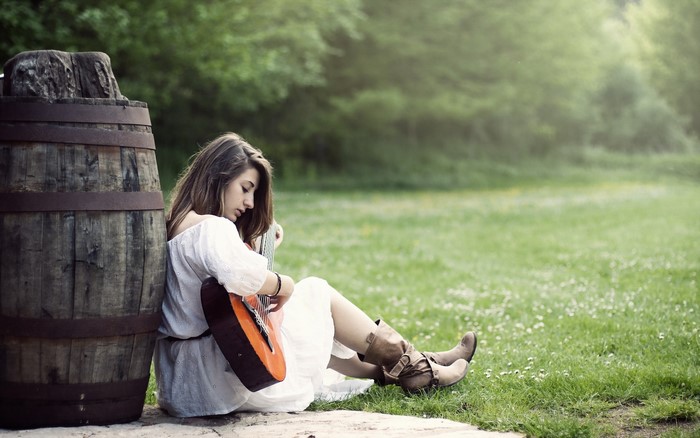 Girl with guitar sitting by a barrel